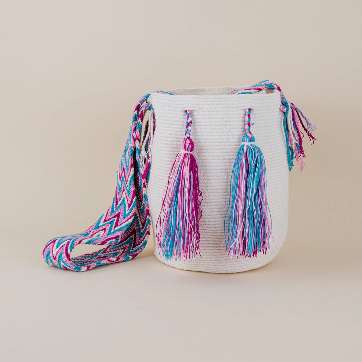 Front view of Calera Wayuu Mochila with white handwoven body, colorful tassels and pink and turquoise woven shoulder strap – Maison Monserrate
