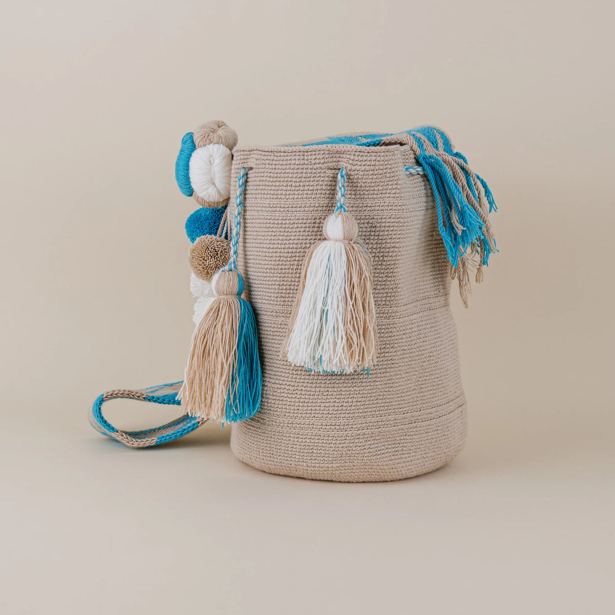 Angled view of Cartagena Wayuu Mochila with beige and turquoise woven strap and handcrafted tassel details – Maison Monserrate