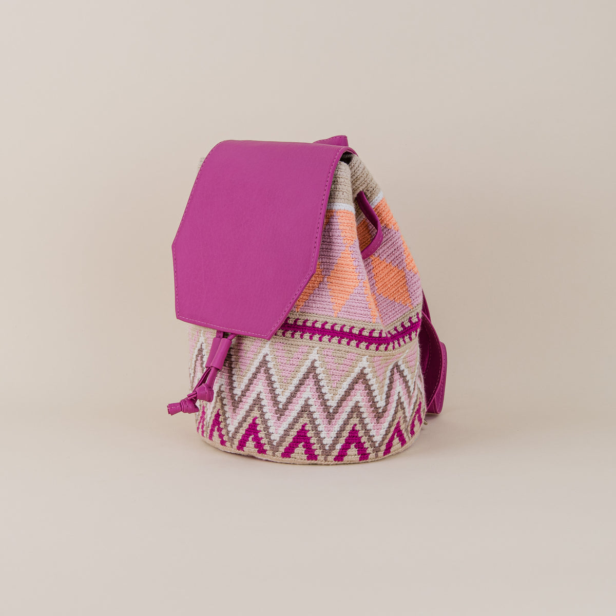 Angled view of Sincelejo Wayuu Backpack showing pink, cream and orange handwoven pattern, fuchsia flap and shoulder straps – Maison Monserrate