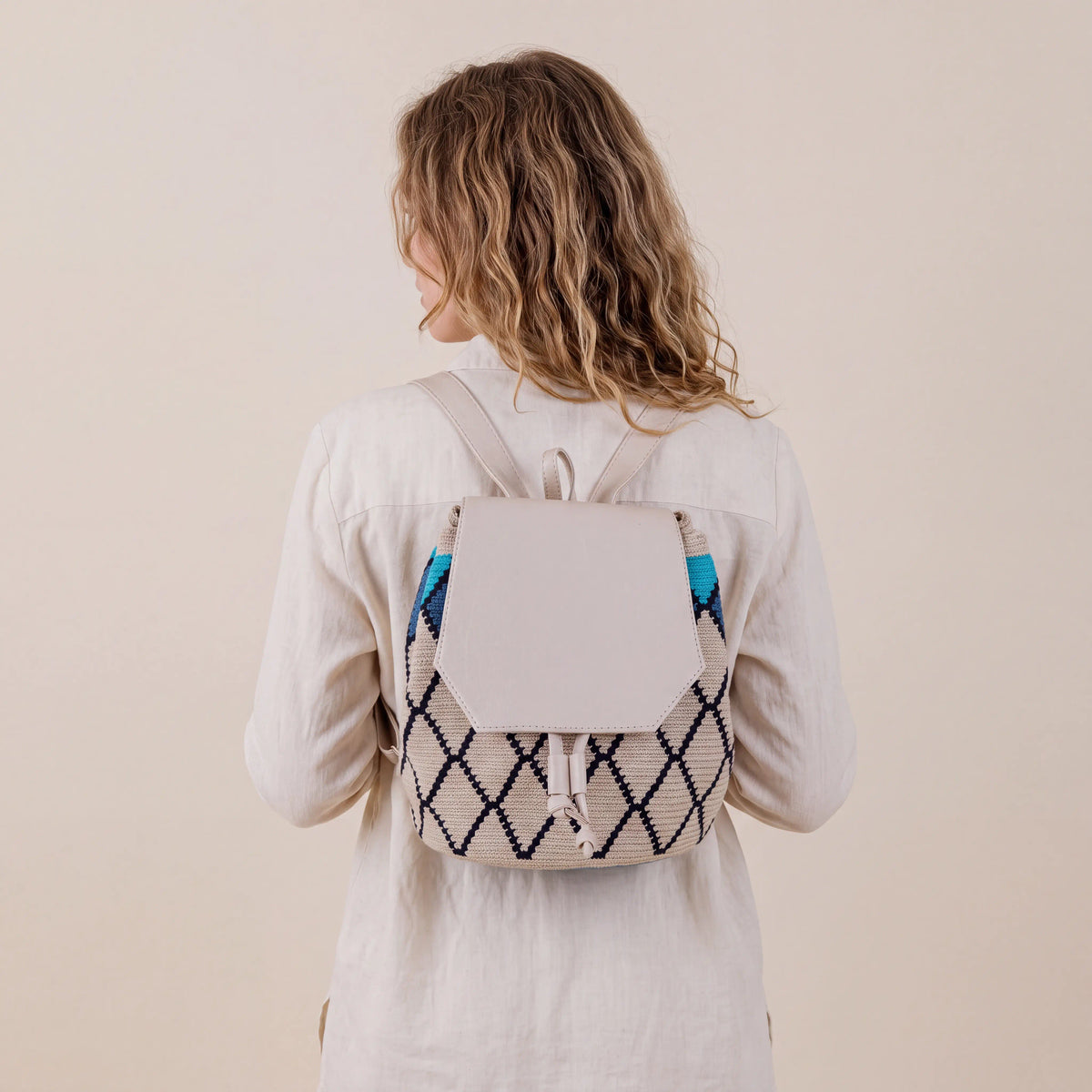 Model wearing Covenas Wayuu Backpack featuring beige, navy blue and turquoise handwoven geometric patterns and a light leather flap – Maison Monserrate