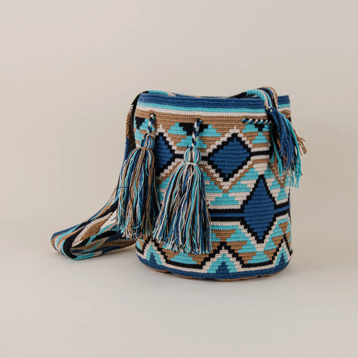 Angled view of Pasto Wayuu Mochila featuring blue and turquoise geometric weaving, tassels and woven shoulder strap – Maison Monserrate